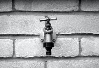 grayscale of metal faucet on wall brick