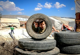 boys looking through car wheel in slum