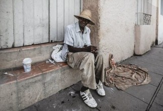 black man in dirty clothes sitting on a street