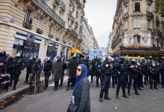 Uma mulher vista passando perto de um esquadrão policial durante o comício de 13 de outubro de 2023 em Paris [Telmo Pinto/SOPA Images/LightRocket via Getty Images]