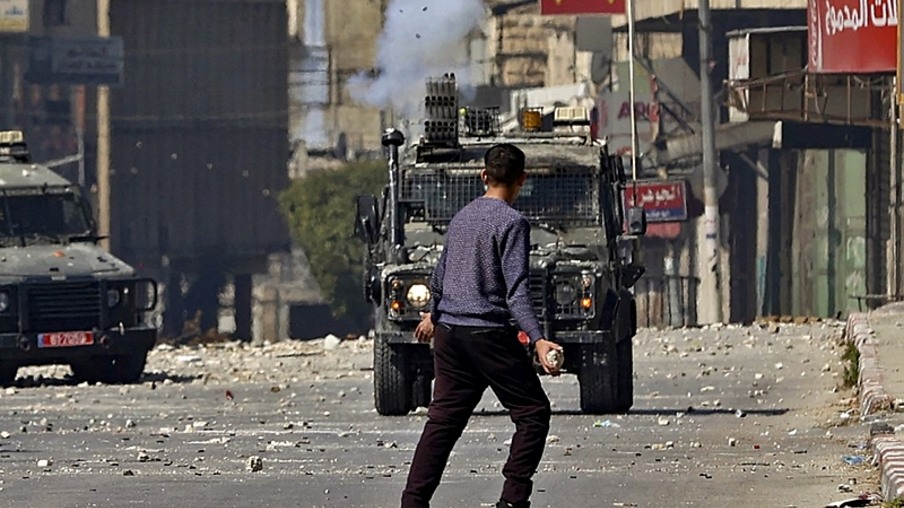 Jovem palestino e comboio militar israelense em Nablus, na Palestina - Zain Jaafar / AFP